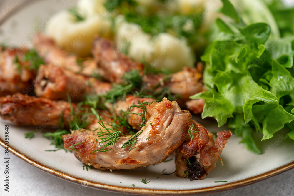 Baked or fried chicken necks in barbecue sauce, cauliflower and lettuce leaves on a plate on the table. A healthy dinner on a light gray background in closeup. Proper nutrition Baked or fried chicken necks in barbecue sauce, cauliflower and lettuce leaves on a plate on the table. A healthy dinner on a light gray background in closeup. Proper nutrition
