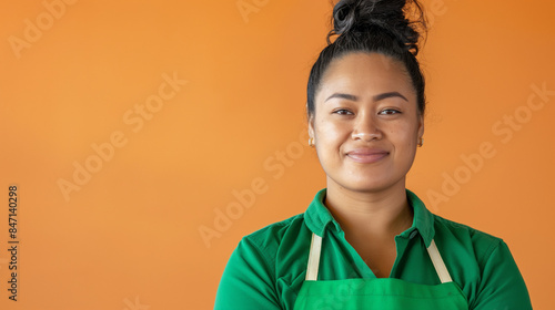 happy young Polynesian woman wearing a green apron looking at the camera against an orange background. female diversity business 