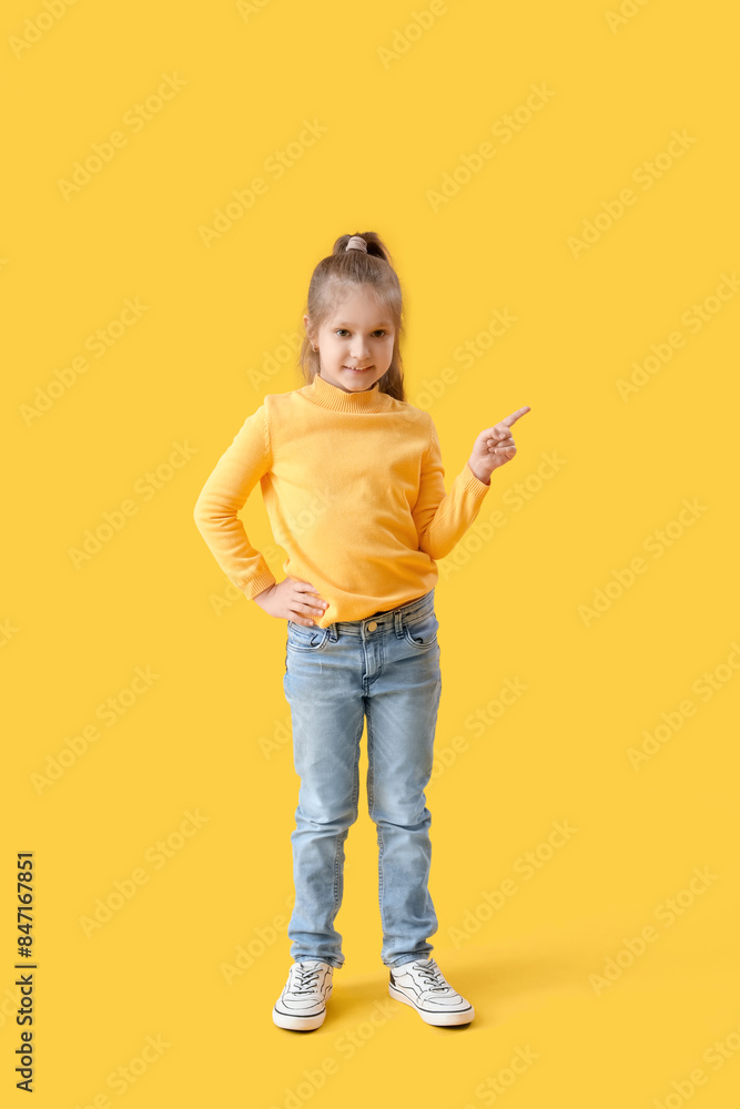 Cute little girl in sweater pointing at something on yellow background Cute little girl in sweater pointing at something on yellow background