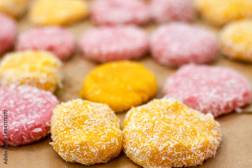 Close-up of yellow and pink raw cookies, ready to bake, in coconut flakes on a baking sheet. Close-up of yellow and pink raw cookies, ready to bake, in coconut flakes on a baking sheet.