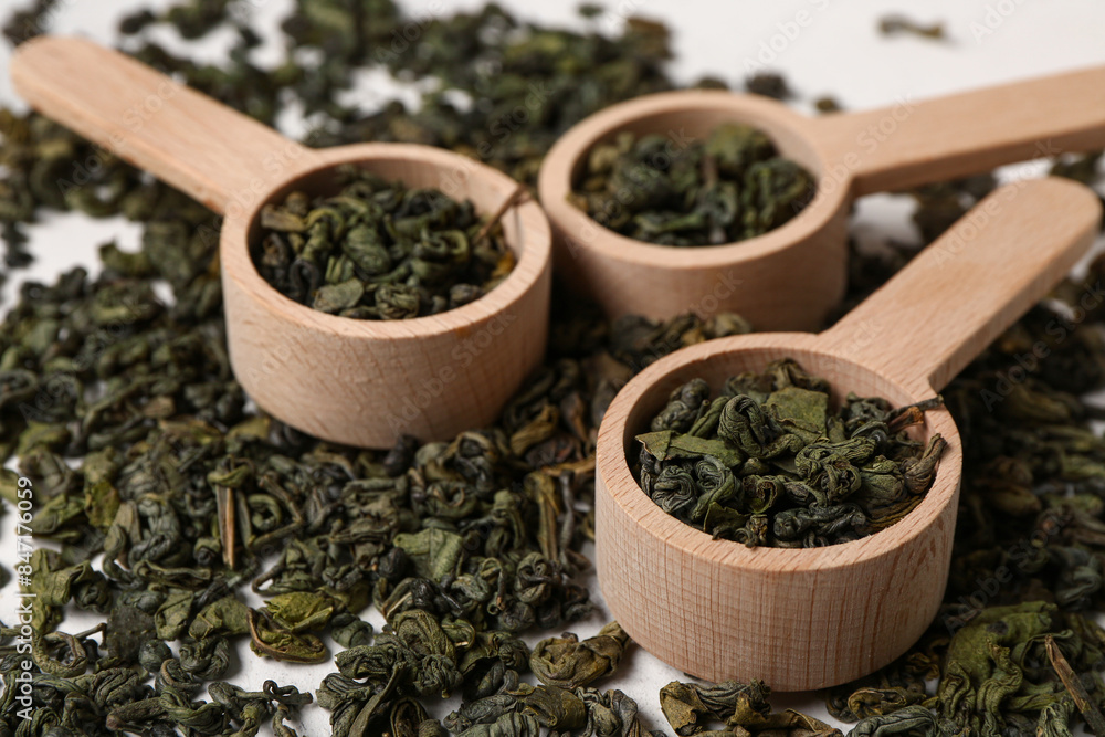 Wooden spoons with dry green tea leaves as background, closeup Wooden spoons with dry green tea leaves as background, closeup