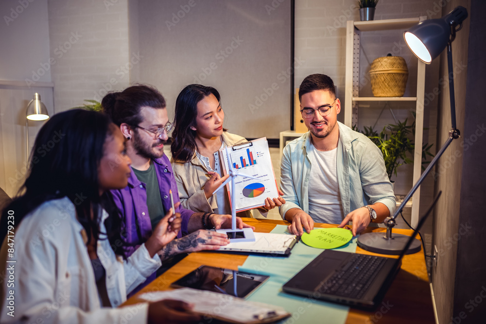 A group of four young people is sitting together at home, collaborating on a project using a laptop, with focused and engaged expressions. A group of four young people is sitting together at home, collaborating on a project using a laptop, with focused and engaged expressions.