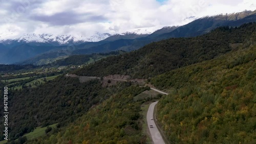 Aerial view of the road among the mountains. The car drives among beautiful and high mountains. All around are mountainous expanses, trees, nature. 4k drone video.