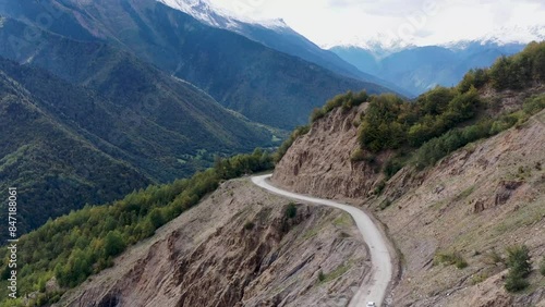 Aerial view of the road among the mountains. The car drives among beautiful and high mountains. All around are mountainous expanses, trees, nature. 4k drone video.