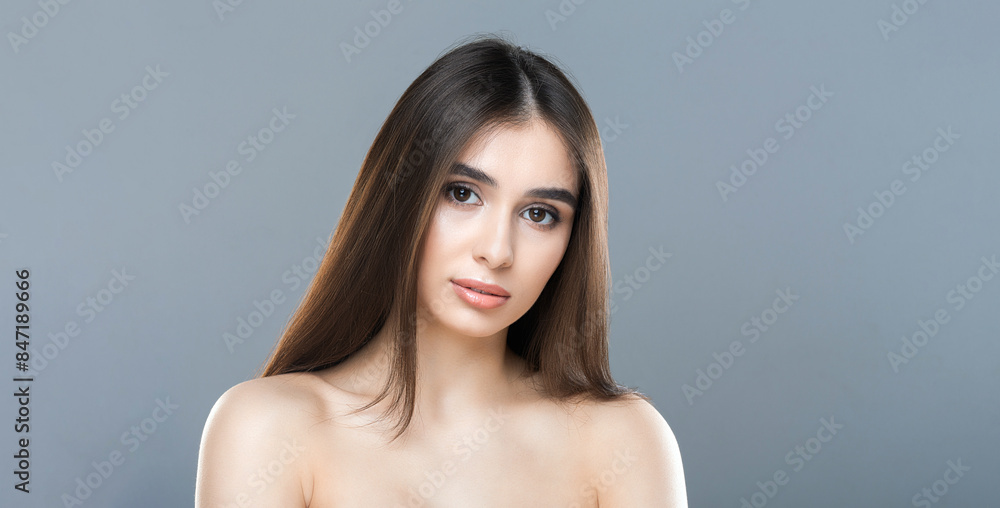 Fototapeta premium A woman with flowing, long hair is striking a pose for a photograph. She appears confident and poised, with one hand on her hip and a slight smile on her face. The background is simple