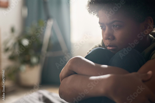 Dramatic close up portrait of Black boy crying and hugging knees in hazy dark room with blurred background copy space photo