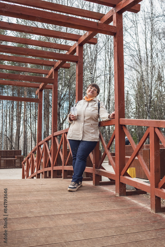 An elderly woman sits on a wooden bridge in a city park. An elderly woman sits on a wooden bridge in a city park.