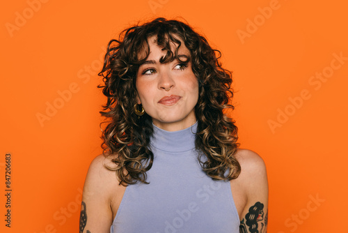 Stylish young woman with tattoos against orange background