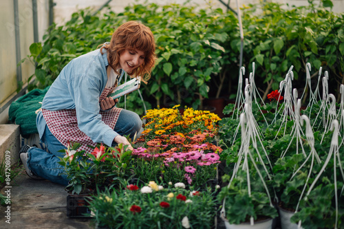 Fotografi Happy botanist with checklist kneeling at hothouse and touching flowers