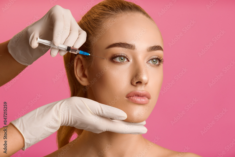 Cosmetology concept. Young woman getting beauty injection near eyes, pink background Cosmetology concept. Young woman getting beauty injection near eyes, pink background