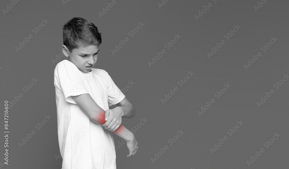 The youngster's face contorted in pain as he touches his elbow, suggesting an injury isolated on grey The youngster's face contorted in pain as he touches his elbow, suggesting an injury isolated on grey