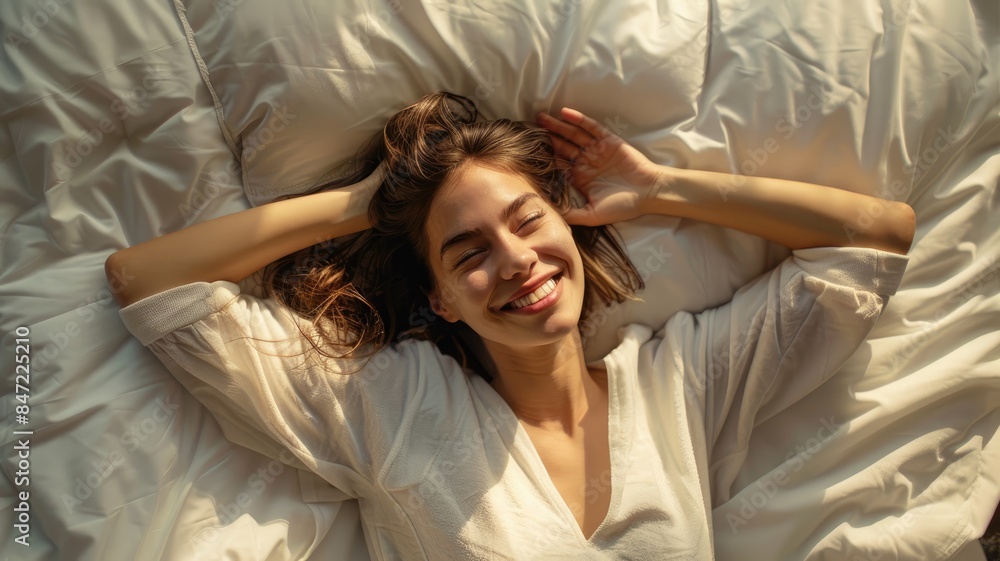 Naklejka premium Top view from above smiling young woman stretching, lying in comfortable bed after awakening, happy positive young female wearing pajama resting on soft pillows under warm blanket, enjoying morning.