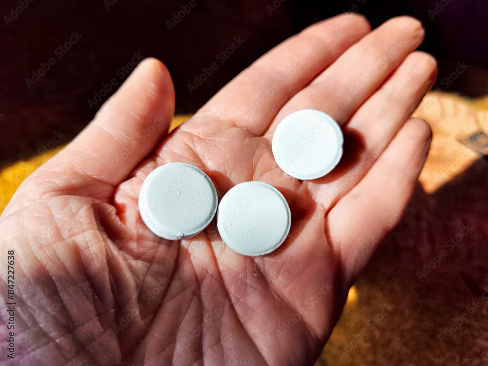 In the soothing natural light, a hand delicately holds three circular white pills In the soothing natural light, a hand delicately holds three circular white pills