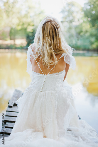 Girl in wedding dress sitting near the water view from the back 