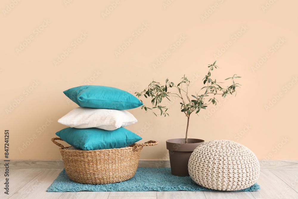 Basket with stylish pillows, pouf and plant near beige wall in room Basket with stylish pillows, pouf and plant near beige wall in room