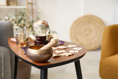 Tibetan singing bowl with witch's magic attributes on table in living room, closeup photo