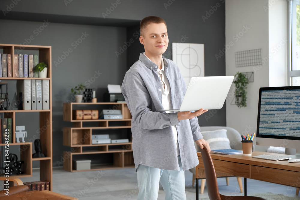 Young male programmer working with laptop and computer in modern home office Young male programmer working with laptop and computer in modern home office