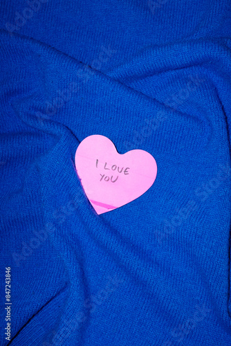 Heart-shaped I love you note on blue background with direct flashlight