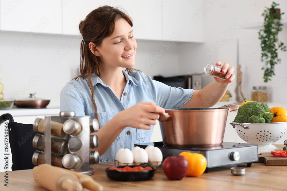 Young woman in wheelchair peppering soup on stove at home Young woman in wheelchair peppering soup on stove at home