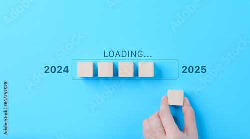 Loading Progress Bar from 2024 to 2025 with Wooden Blocks. A hand places wooden blocks in a row, creating a progress bar transitioning from 2024 to 2025, symbolizing the new year and future progress. photo