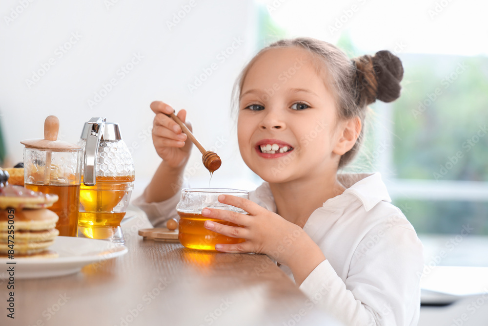Cute little girl eating honey at table in kitchen