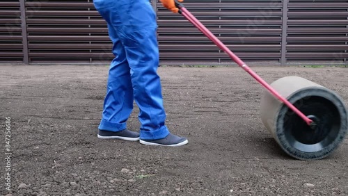 male worker in a uniform prepares a plot of land for sowing a lawn using a lawn roller, leveling and compacting the earth	