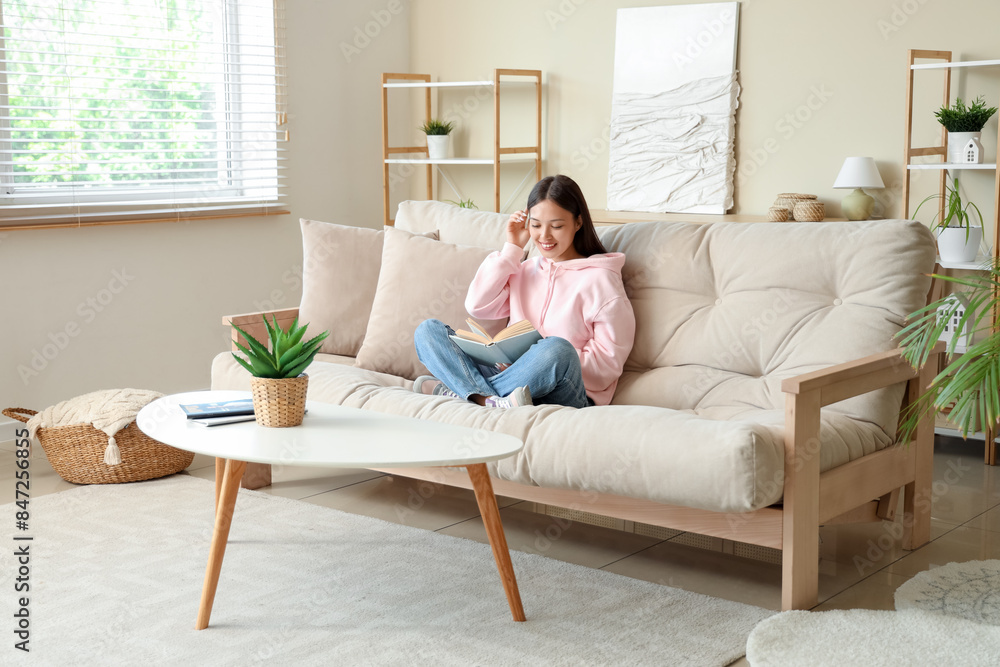 Beautiful young woman reading book and sitting on couch at home Beautiful young woman reading book and sitting on couch at home