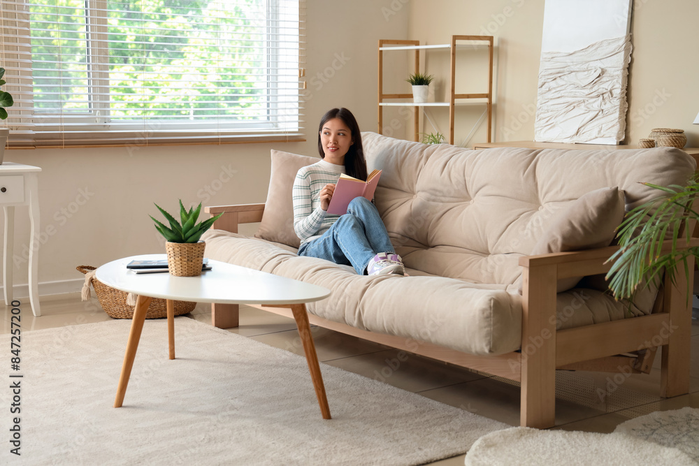 Beautiful young woman reading book on couch at home Beautiful young woman reading book on couch at home
