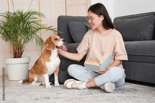 Young woman reading book and sitting with adorable Beagle dog on floor in living room