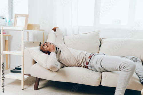 Stressed African American man with a headache sitting alone on the couch at home He appears tired, sick, and depressed, reflecting the mental and physical toll of stress and anxiety on his health The