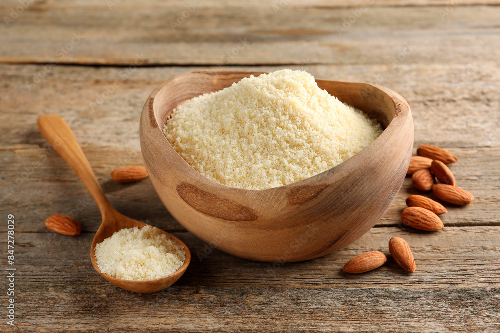 Fresh almond flour in bowl, spoon and nuts on wooden table, closeup Fresh almond flour in bowl, spoon and nuts on wooden table, closeup