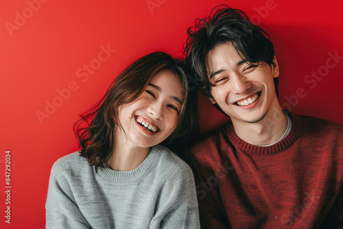 Happy East Asian Couple isolated on a red Background China Japan Korea Smiling Embracing Love Joyful Cheerful Portrait Studio Photography Relationship Togetherness © Magnimage