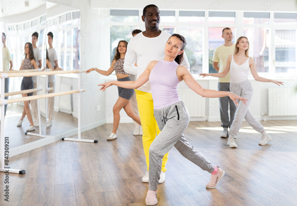 Fototapeta premium Smiling African american man and female partner with multinational group active people training energetic and fast twist or charleston dance movements in modern dance salon