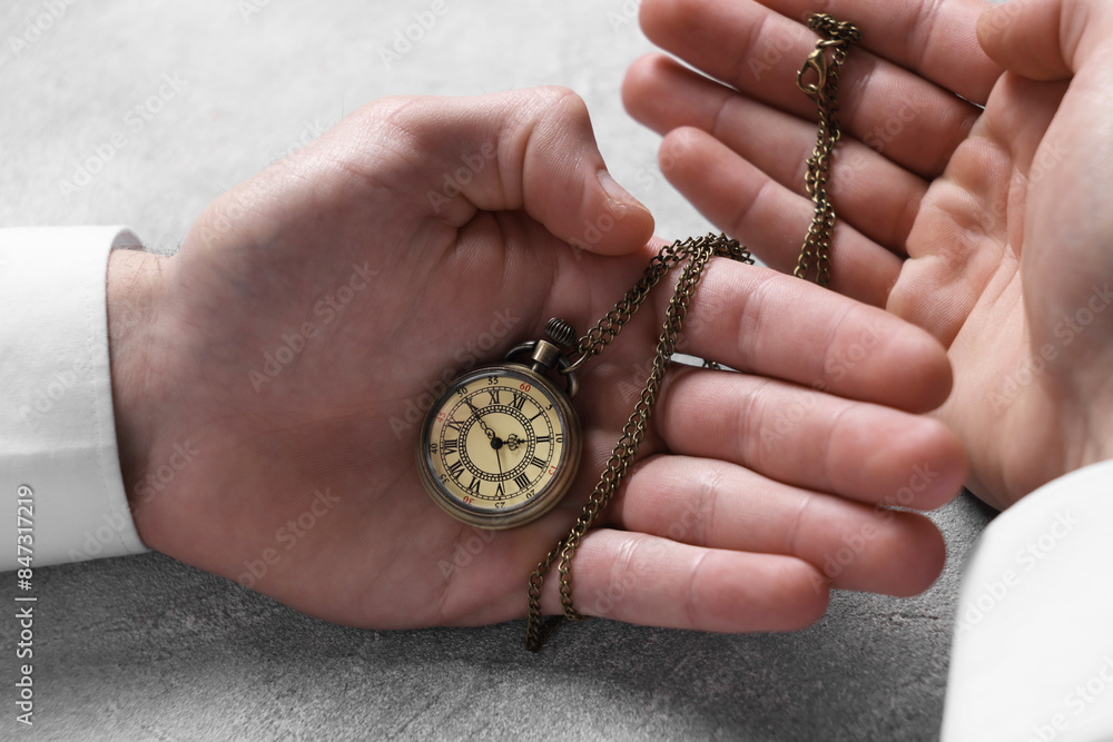 Man holding chain with elegant pocket watch at grey textured table, closeup Man holding chain with elegant pocket watch at grey textured table, closeup