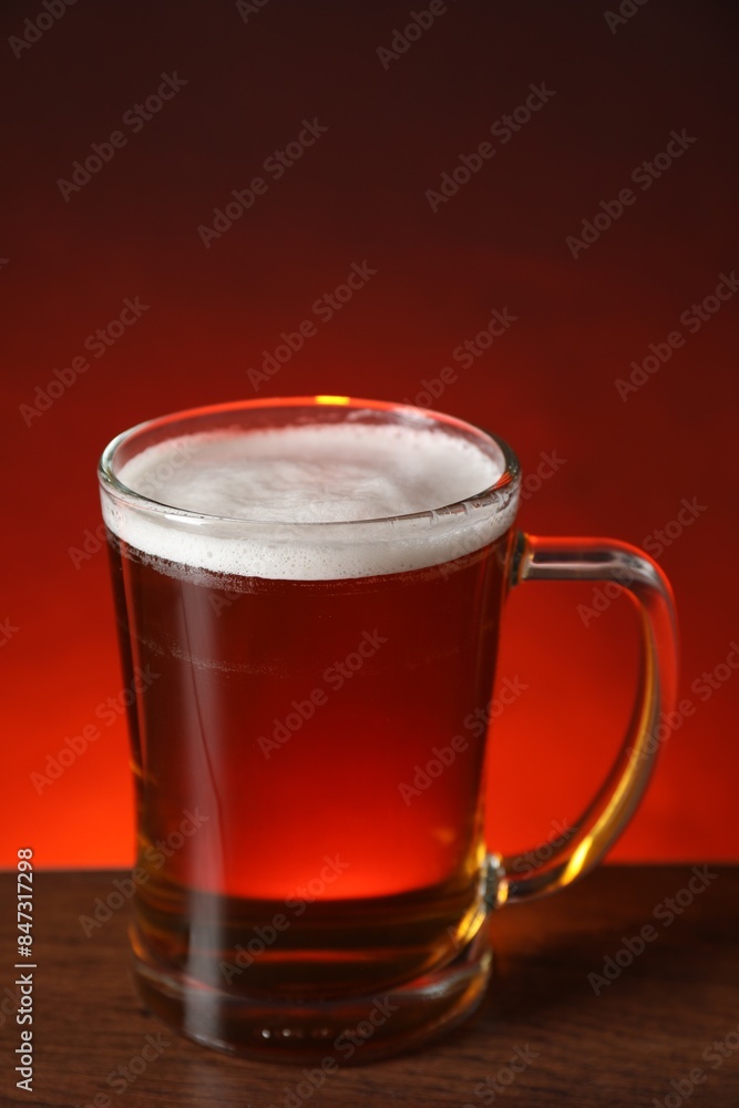 Mug with fresh beer on wooden table against color background Mug with fresh beer on wooden table against color background