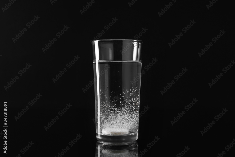 Effervescent pill dissolving in glass of water on black background Effervescent pill dissolving in glass of water on black background