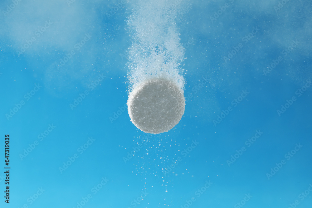 Fototapeta premium Effervescent pill dissolving in water on light blue background, closeup