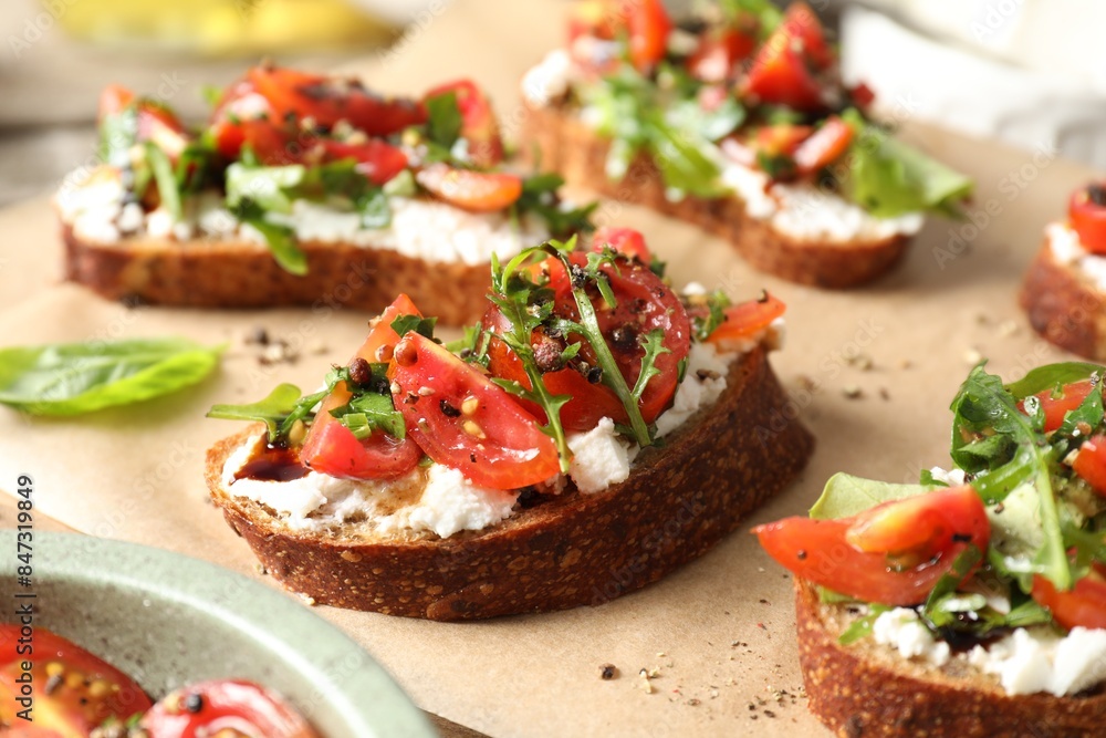 Delicious ricotta bruschettas with tomatoes and arugula on parchment, closeup Delicious ricotta bruschettas with tomatoes and arugula on parchment, closeup