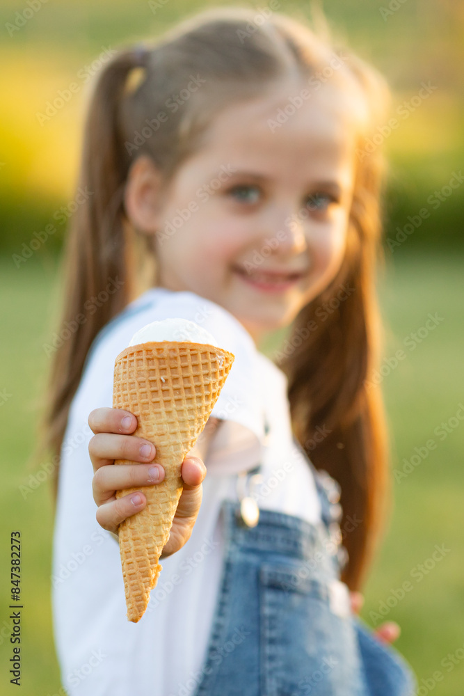 An ice cream in the hand of happy laughing child in summer clothes on a hot day in park. Ice cream in a waffle cone. A happy and contented child at summer. Selective focus on ice cream An ice cream in the hand of happy laughing child in summer clothes on a hot day in park. Ice cream in a waffle cone. A happy and contented child at summer. Selective focus on ice cream