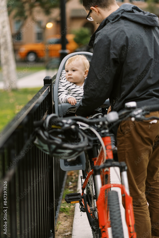 father putting infant son into bike carrier father putting infant son into bike carrier