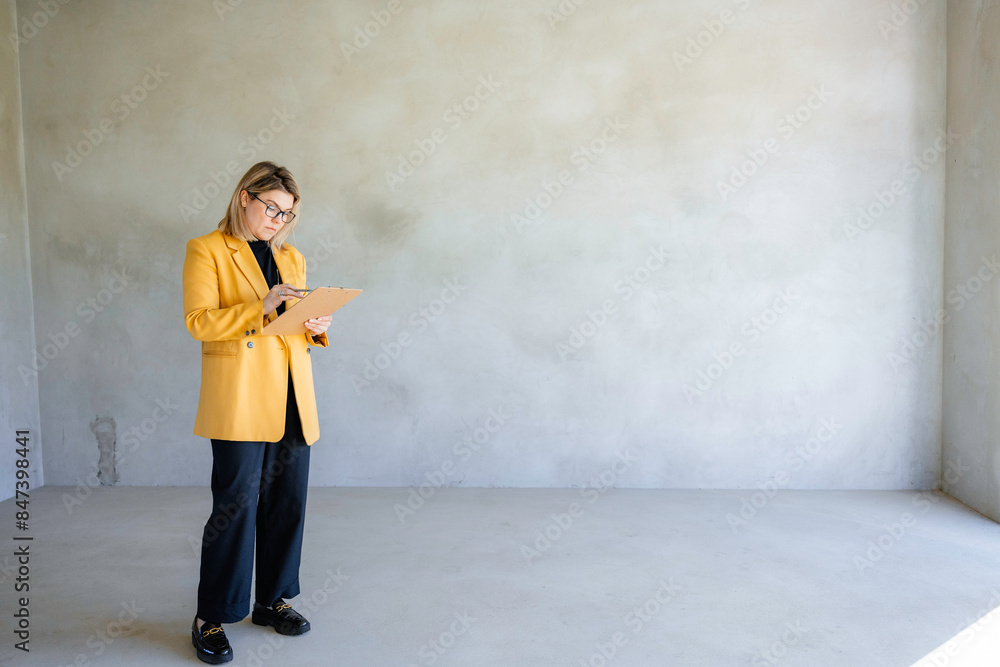 The real estate agent writes in a notebook standing indoors The real estate agent writes in a notebook standing indoors
