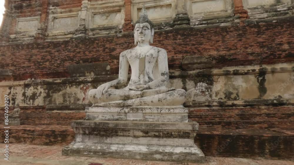 Ancient Buddha statue in meditation pose against a weathered brick wall of a historic temple. Ancient Buddha statue in meditation pose against a weathered brick wall of a historic temple.