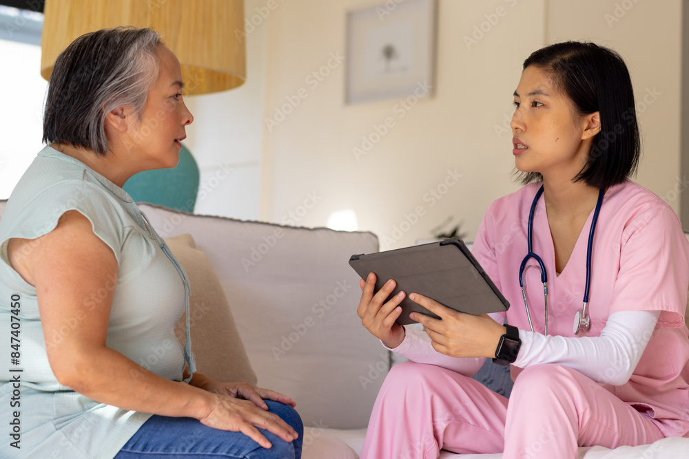 Asian senior woman interacts with an nurse healthcare worker holding a tablet at home Asian senior woman interacts with an nurse healthcare worker holding a tablet at home