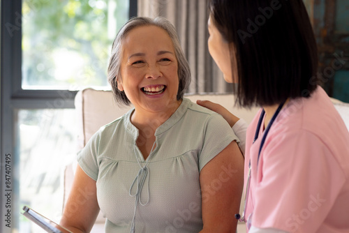 Asian senior woman smiling, talking to younger Asian woman in pink uniform at home