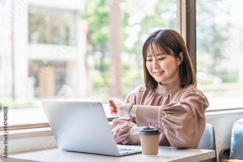 カフェでパソコンを使いながら腕時計を確認する日本人ビジネスウーマン 