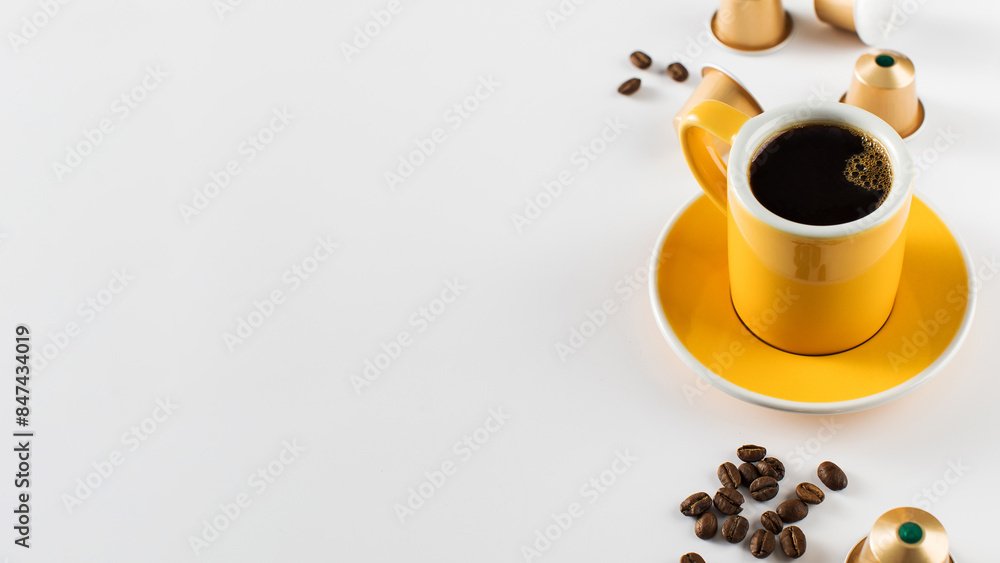 Obraz premium Yellow coffee cup with golden coffee capsules and beans on a white background. Copy space