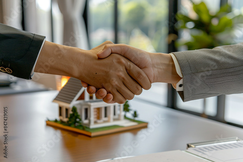 A professional handshake between an estate agent and a customer in an office, with a detailed house model on the desk.