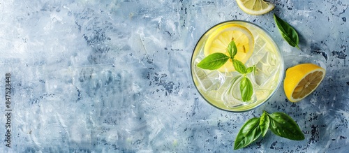 Refreshing summer drink with basil and lemon in a glass on a light blue slate, stone, or concrete backdrop. Overhead shot with space for text.