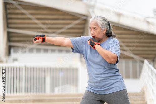 Asian senior sportswoman boxing while working out on parking outdoors