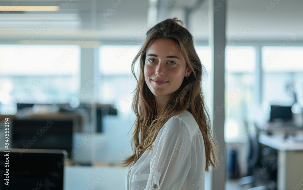 Fototapeta premium A woman with long brown hair and a white shirt is smiling in front of a window. Concept of happiness and positivity